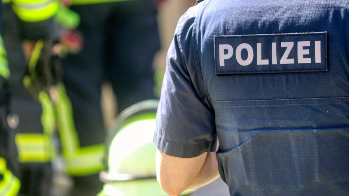 Der Rücken eines Polizisten mit der Aufschrift "Polizei". Neben ihm befindet sich ein verschwommen im Hintergrund jemand von der Feuerwehr und ein entsprechender Helm.