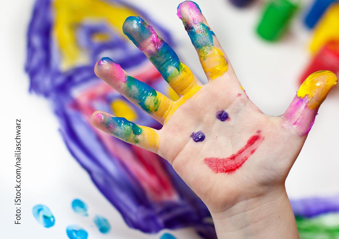 Eine Hand mit bunten Fingerfarben und lachendem Gesicht.