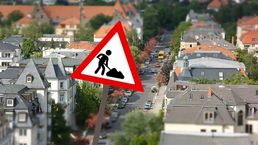 Im Hintergrund ist eine Straße in einer Siedlung mit Straßen, Bäumen und Häusern zu sehen. Im Vordergrund befindet sich als Grafik das Verkehrszeichen "Achtung Baustelle".